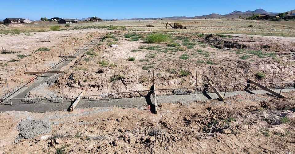 Construction site with freshly poured concrete foundation in a dirt field. Wooden supports along the concrete.