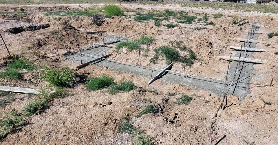 Foundation construction site with concrete footings and wooden forms in a dirt lot.