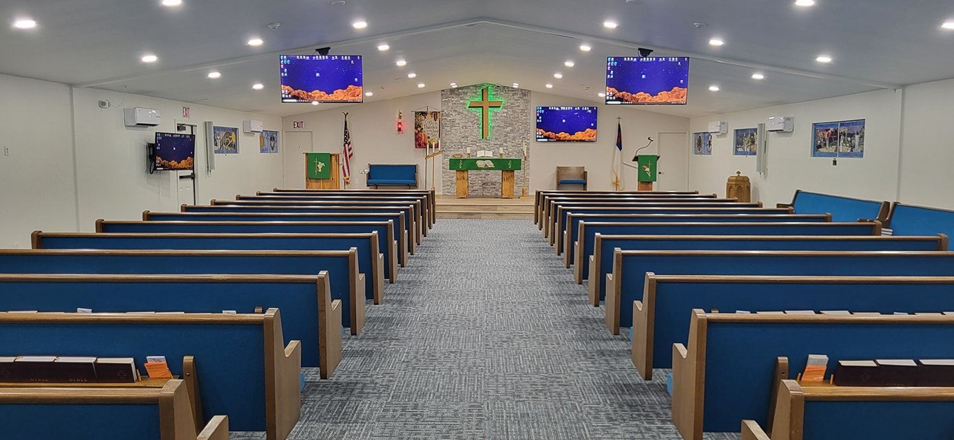 Interior of a church with blue pews facing an altar. Two screens hang on either side.