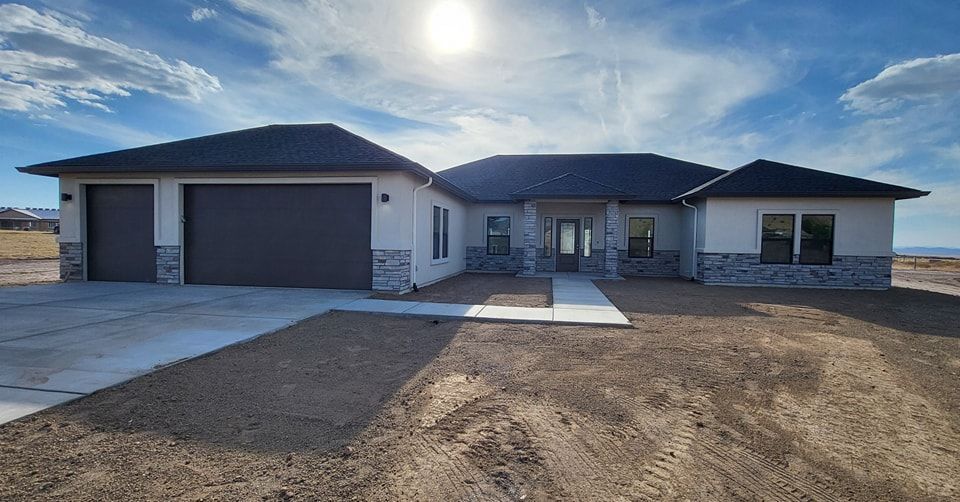 Modern single-story house with gray roof, stone accents, two-car garage, and blue sky.