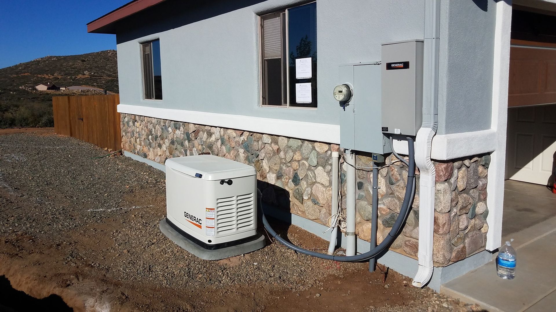A generator next to a house with a stone veneer and electrical panel.