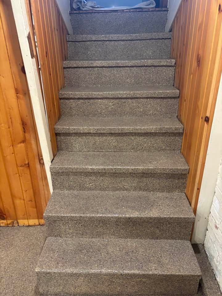 Staircase with gray carpeted steps and wood paneling on the walls.