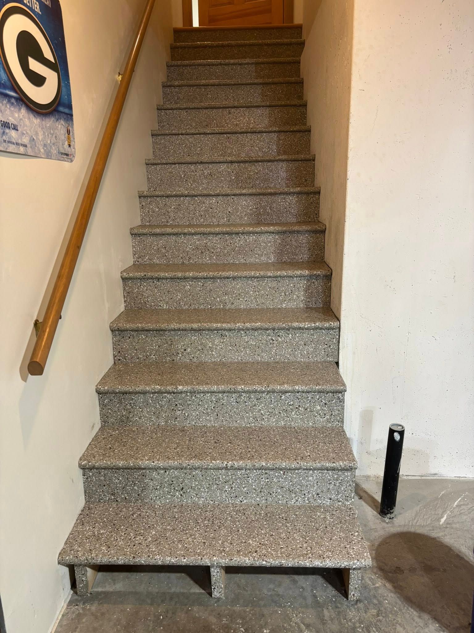 Staircase with gray speckled treads, wooden handrail on the left, leading upwards. Walls are beige and gray.