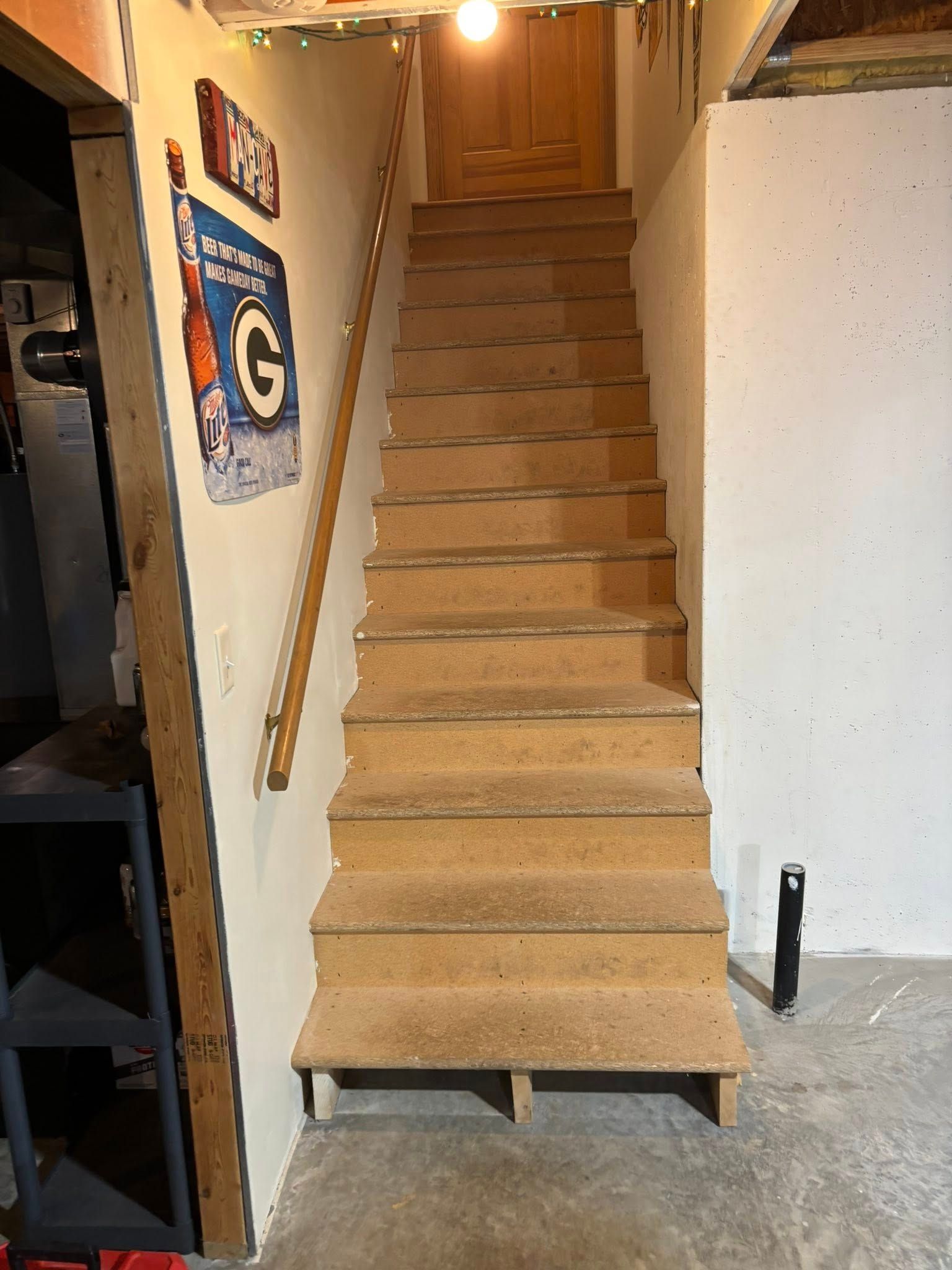 Staircase leading upwards to a wooden door. Handrail on the left. Steps are light brown.