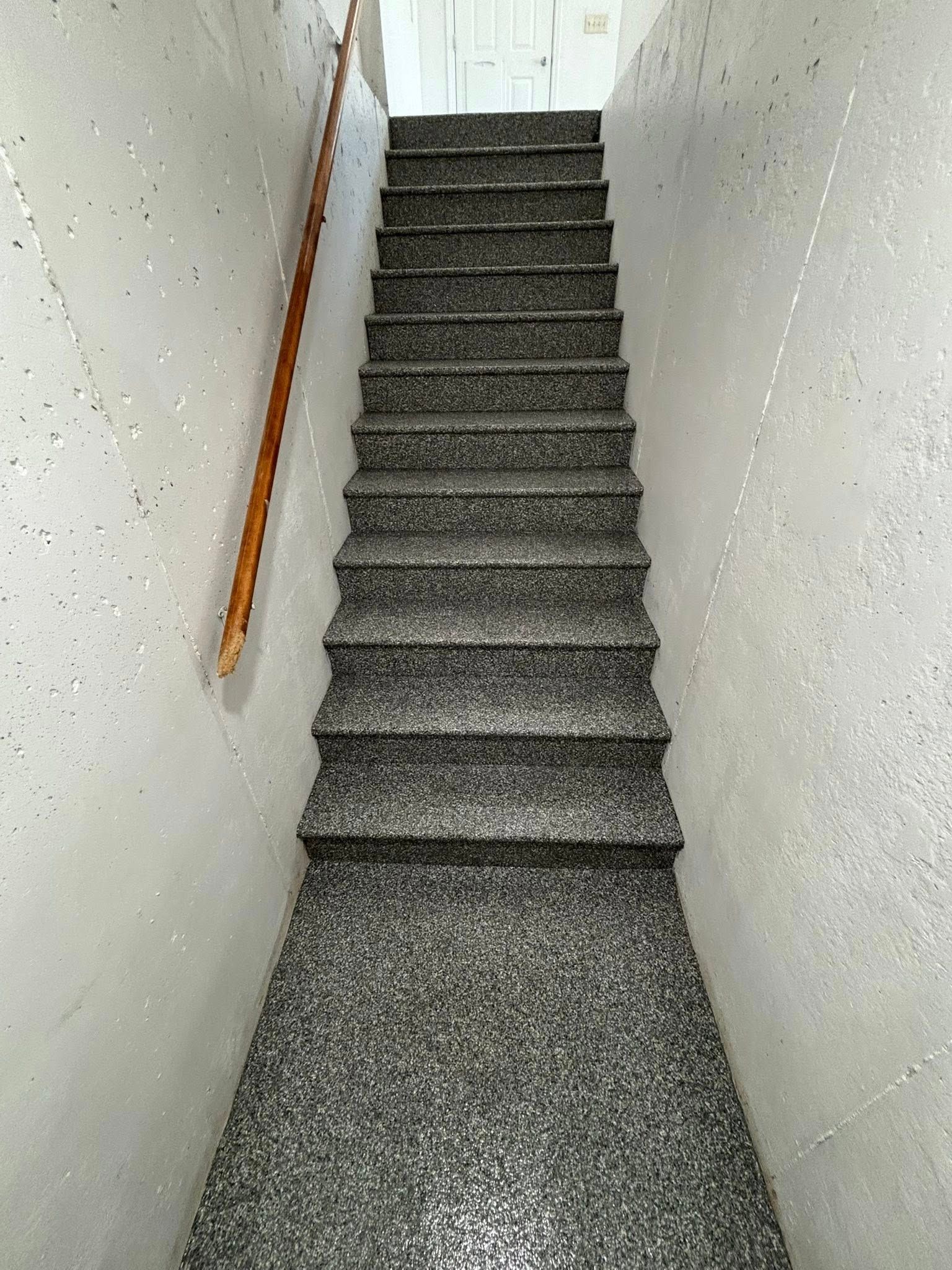 Staircase with gray speckled steps and a wooden handrail on a light gray wall.