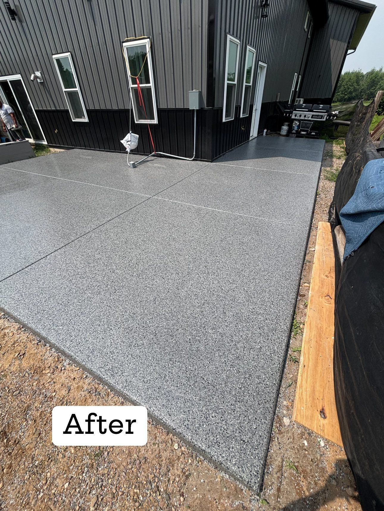 Newly coated concrete patio next to a black house with windows. The coating has a speckled gray finish.