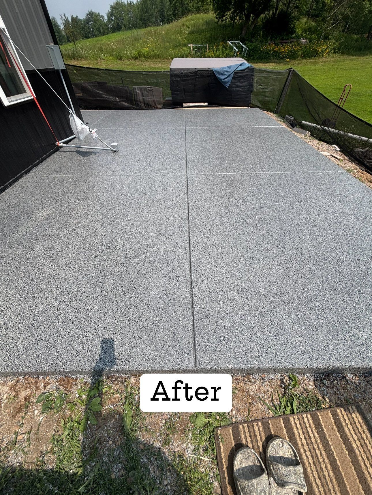 A freshly resurfaced concrete patio with a gray, speckled finish, next to a house and grassy yard.