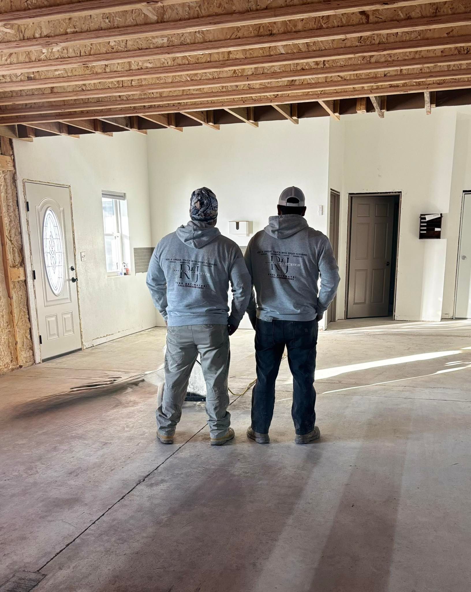 Two men in hoodies stand in a construction site with exposed ceiling beams and unfinished walls.