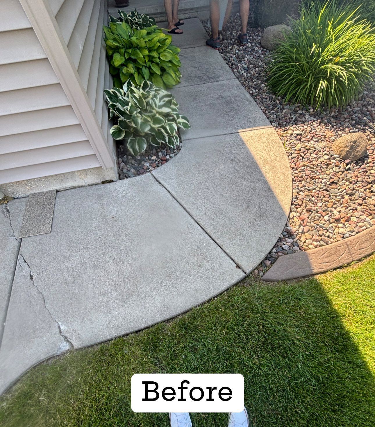 Concrete walkway leading to a house entrance, surrounded by grass and plants, labeled 