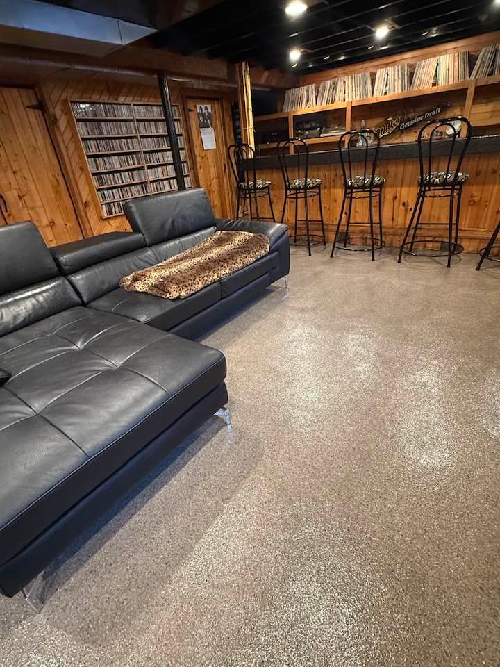 A black leather sectional sofa in a wood-paneled basement with a bar and stools.