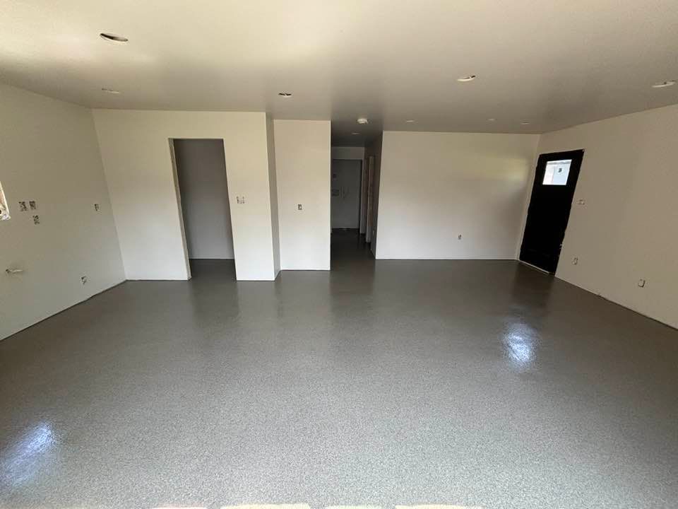 Empty room with gray speckled floor, white walls, and a black door.
