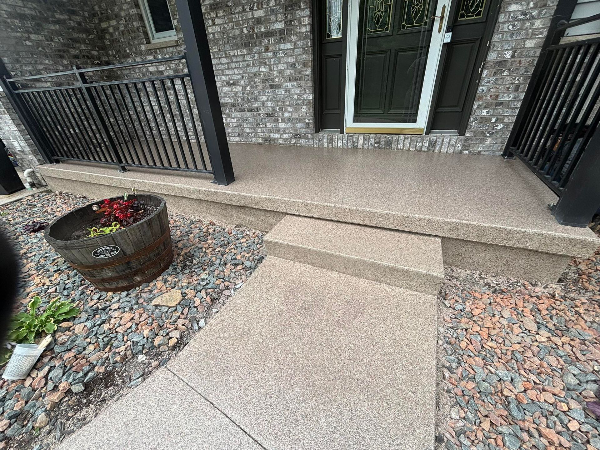 Concrete front porch with steps, dark railings, and a barrel planter.