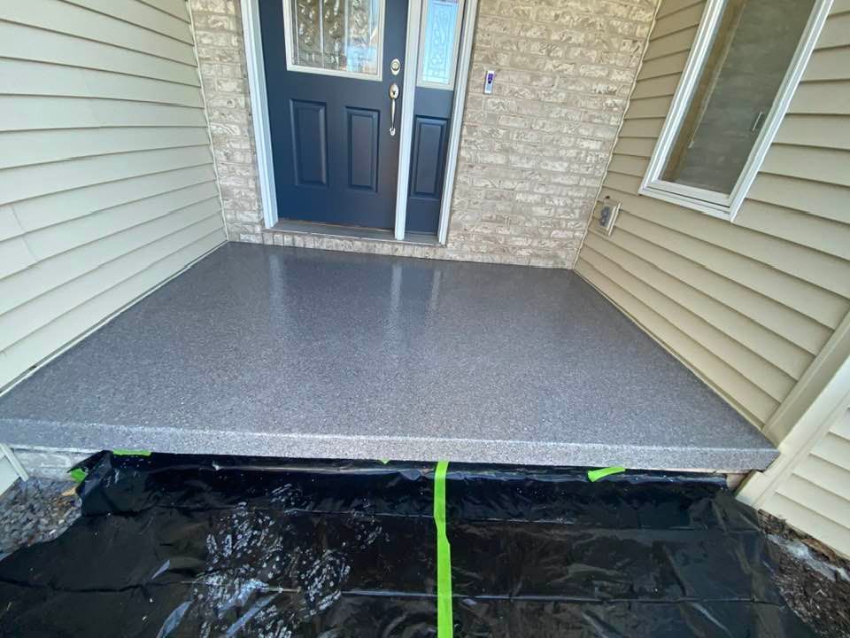 Newly finished gray epoxy porch, black door, beige siding, brick accent.