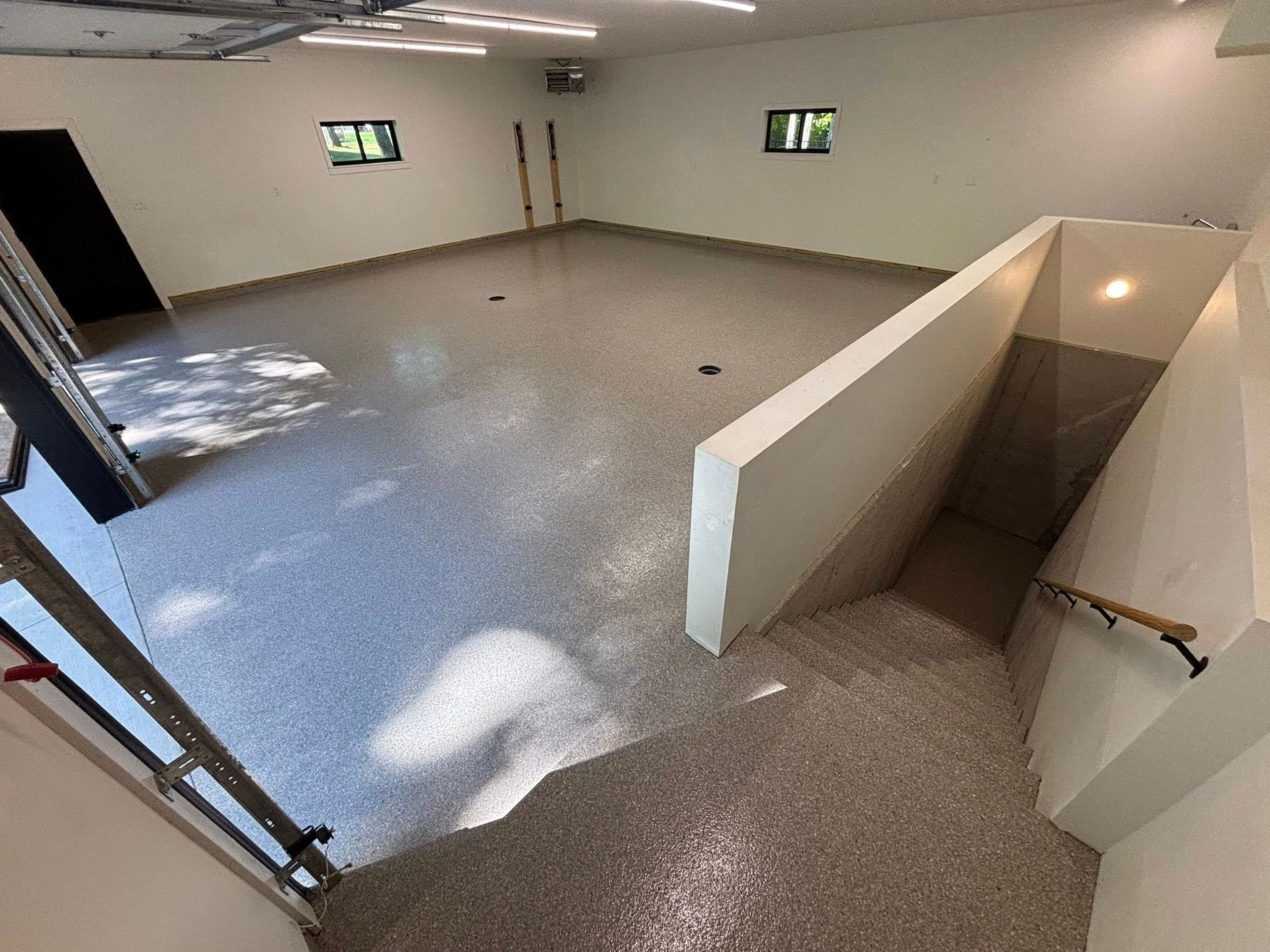 Garage interior with speckled floor, white walls, and a stairway leading down.
