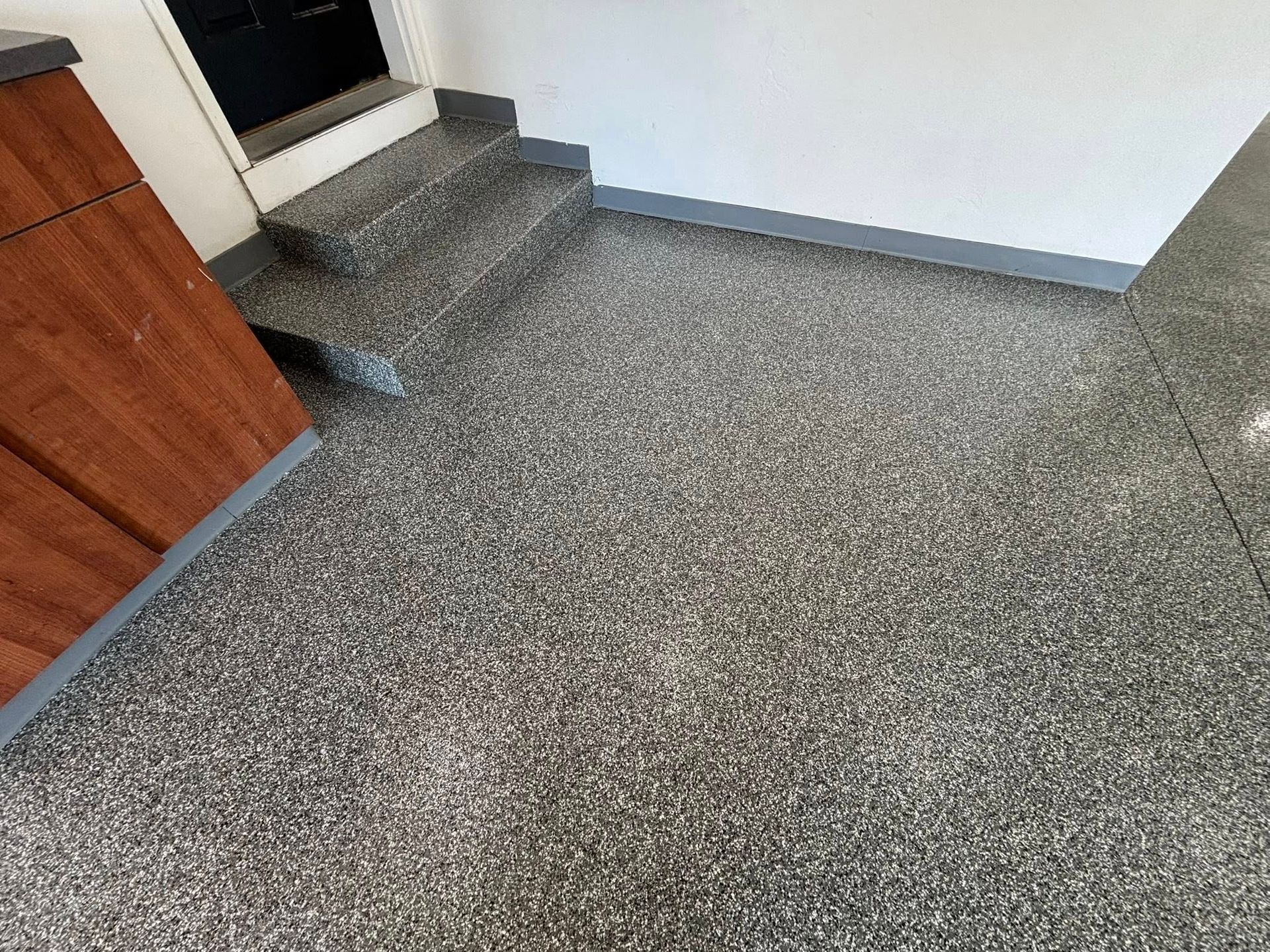 Garage floor with gray speckled epoxy coating and a small set of stairs.