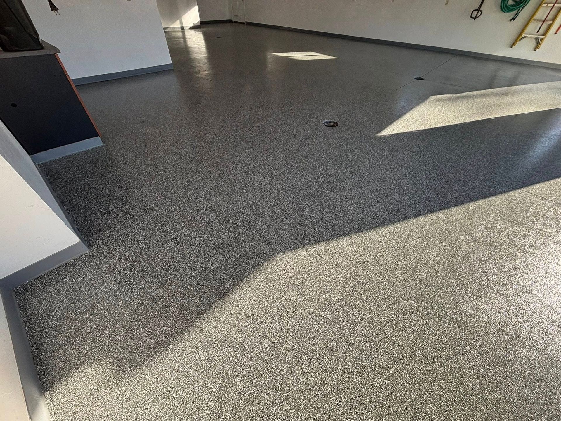 Epoxy-coated garage floor with gray and white chips reflecting sunlight.