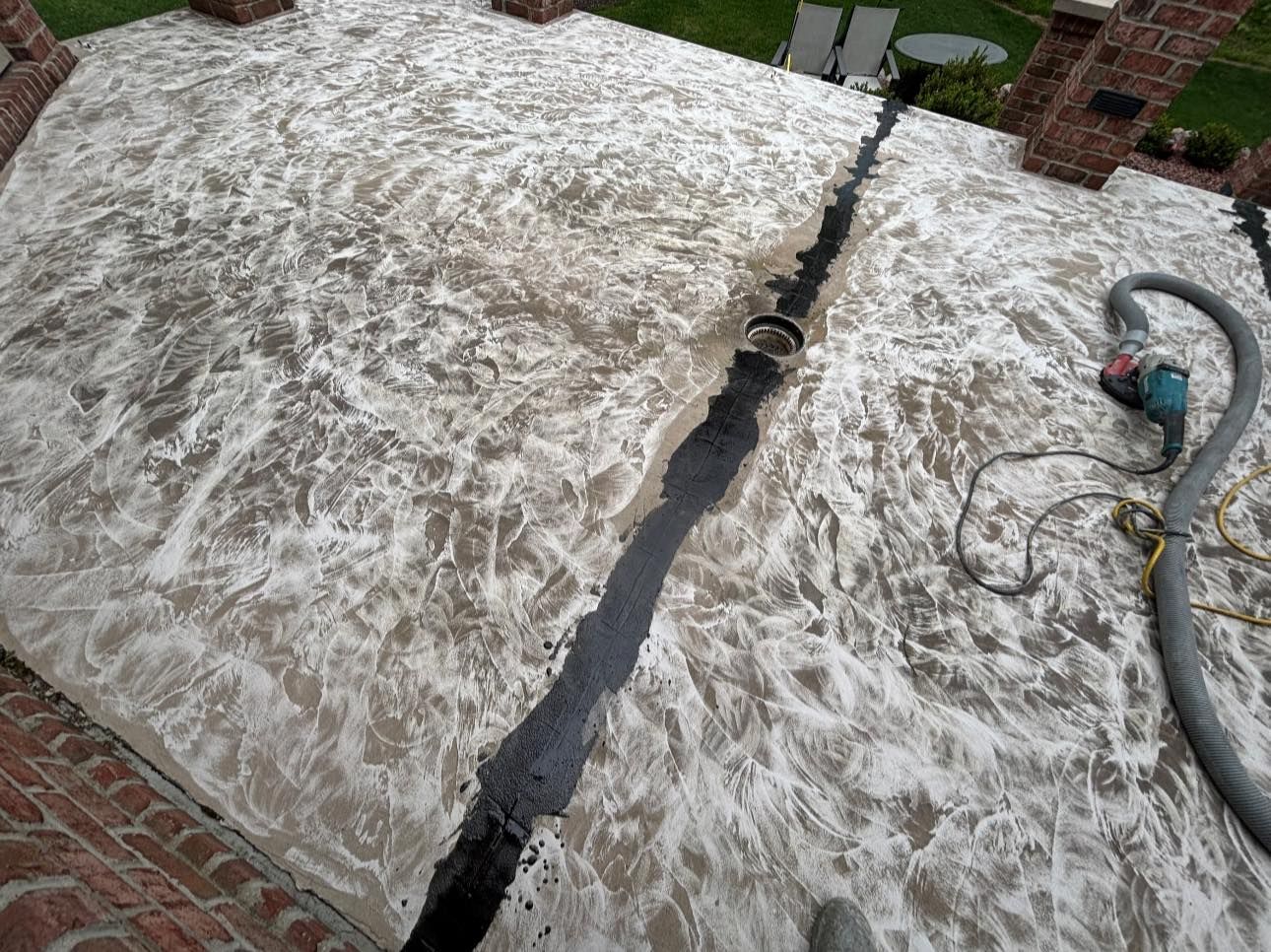 A concrete surface being cleaned. A black crack runs down the center, a hose and vacuum are visible.
