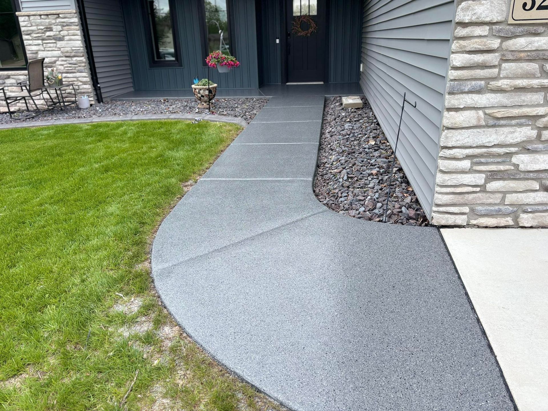Concrete walkway leading to a house with a gray exterior and stone accents.