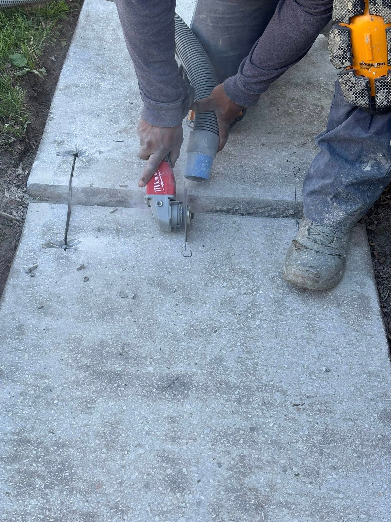 Person using a grinder to cut a line in a concrete sidewalk.