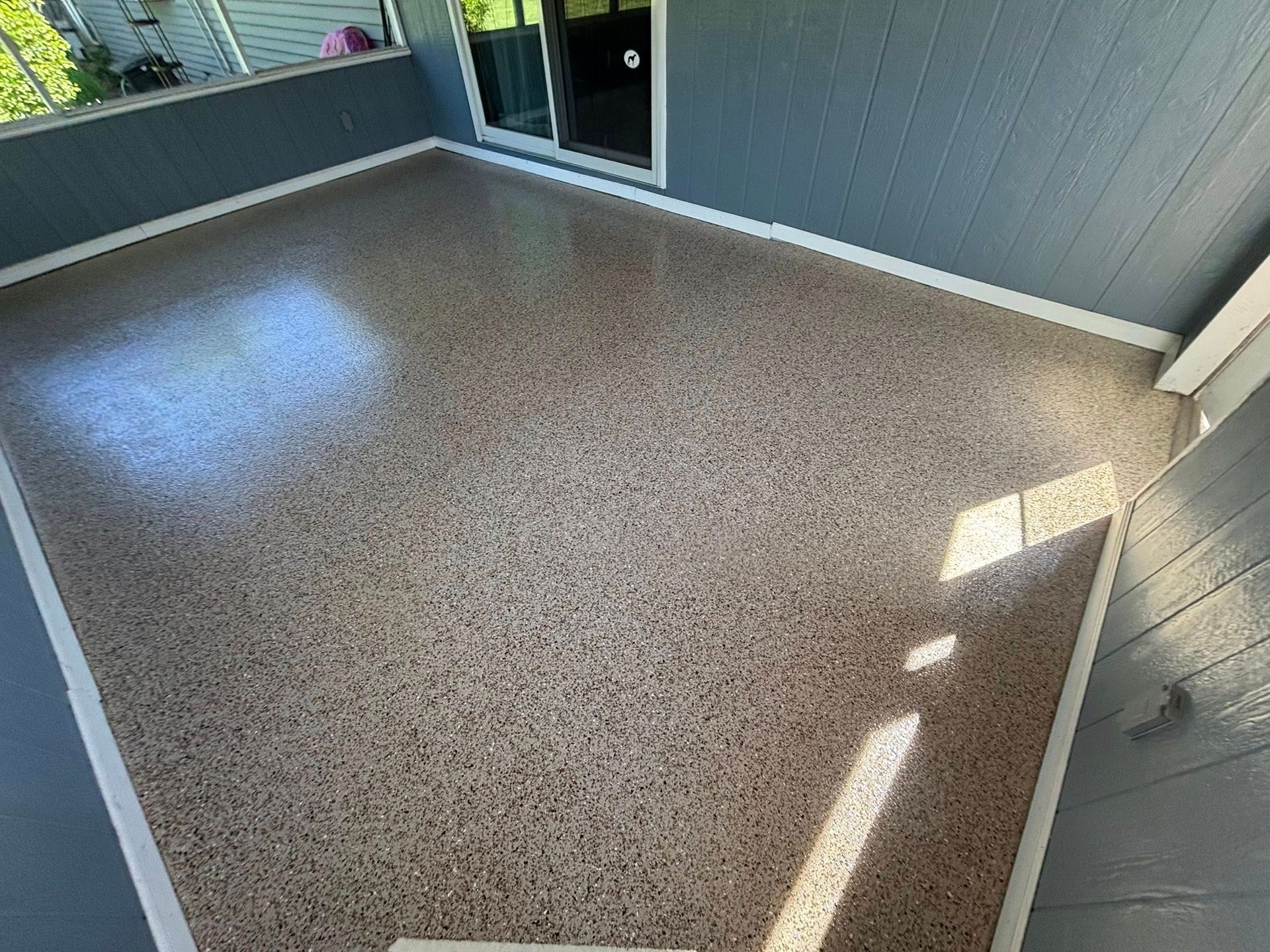 Finished concrete patio with tan flecks, white trim, and a sliding door.