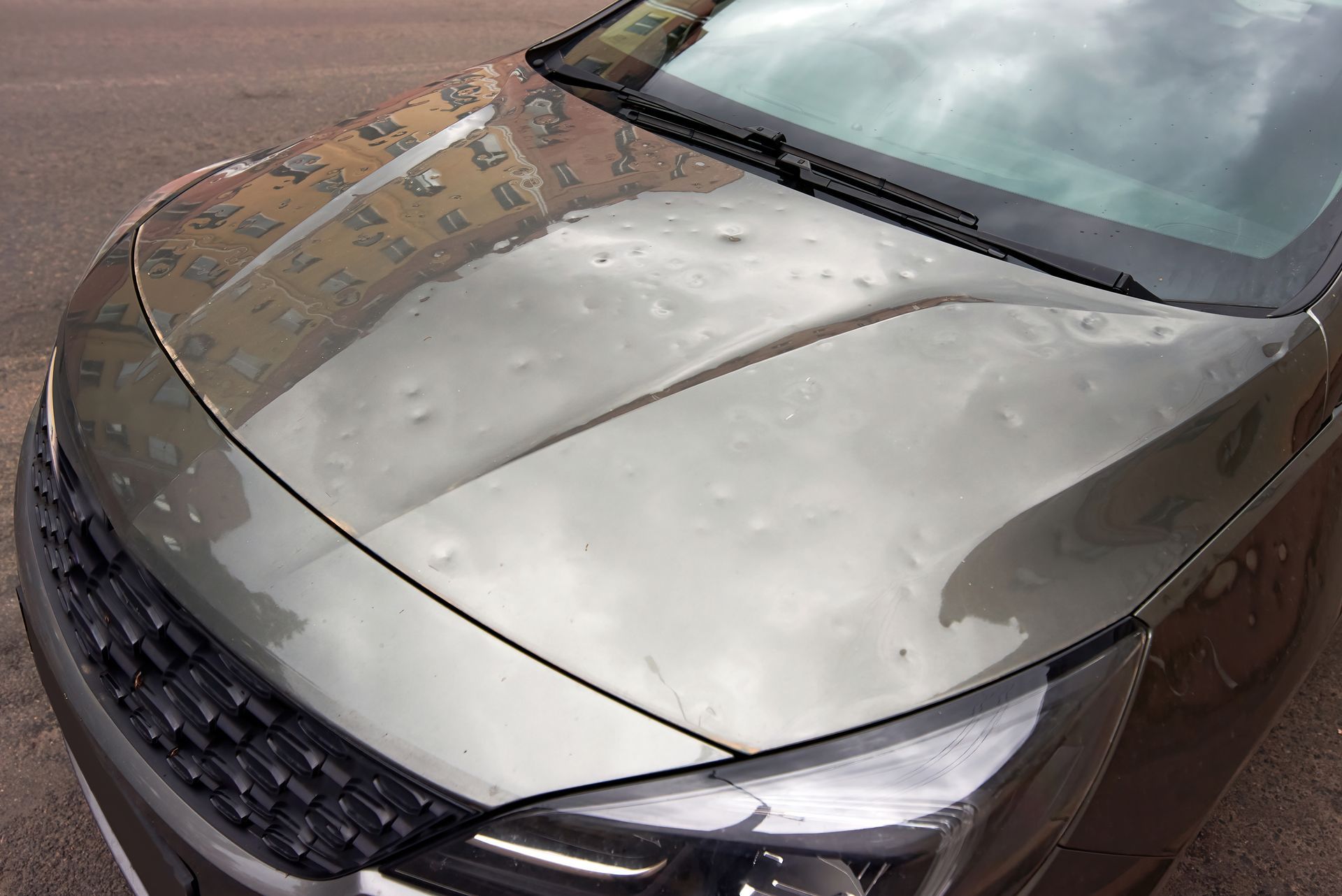 Car hood marked by hail dents, outdoor scene with sky and building reflections. Car hood marked by hail dents, outdoor scene with sky and building reflections.