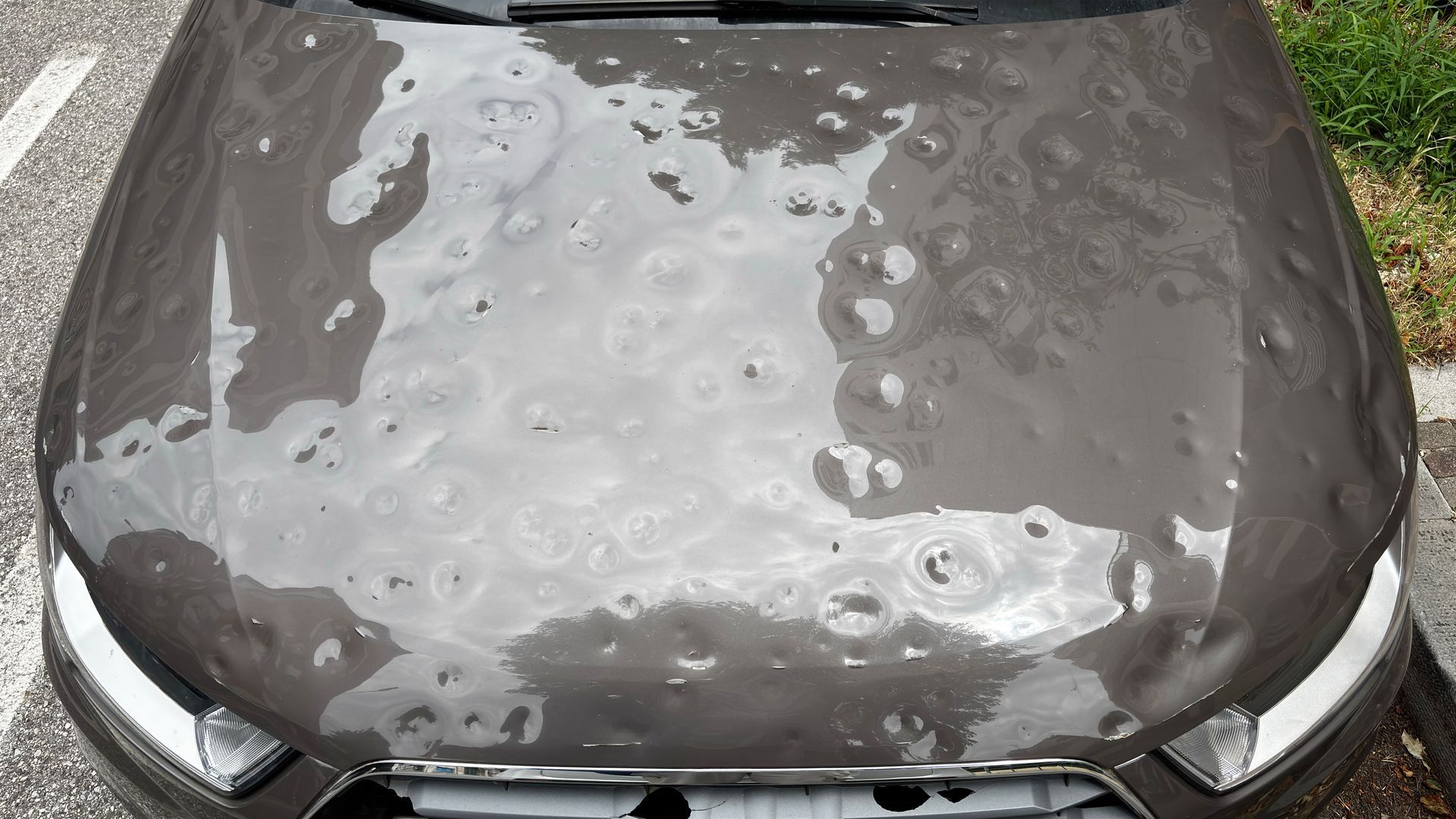 Car hood with heavy hail damage, showing multiple dents and surface impact marks. Car hood with heavy hail damage, showing multiple dents and surface impact marks.