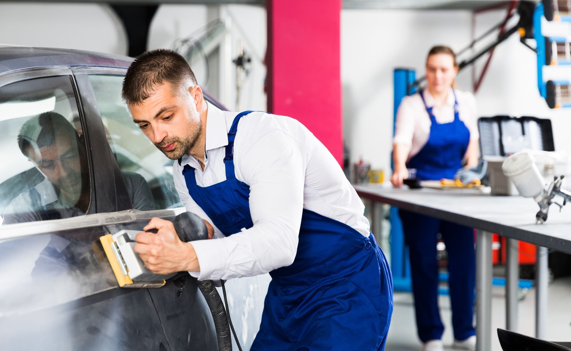 A man with blue overalls polishes a car at Freeman Collision Center, a trusted collision repair cent