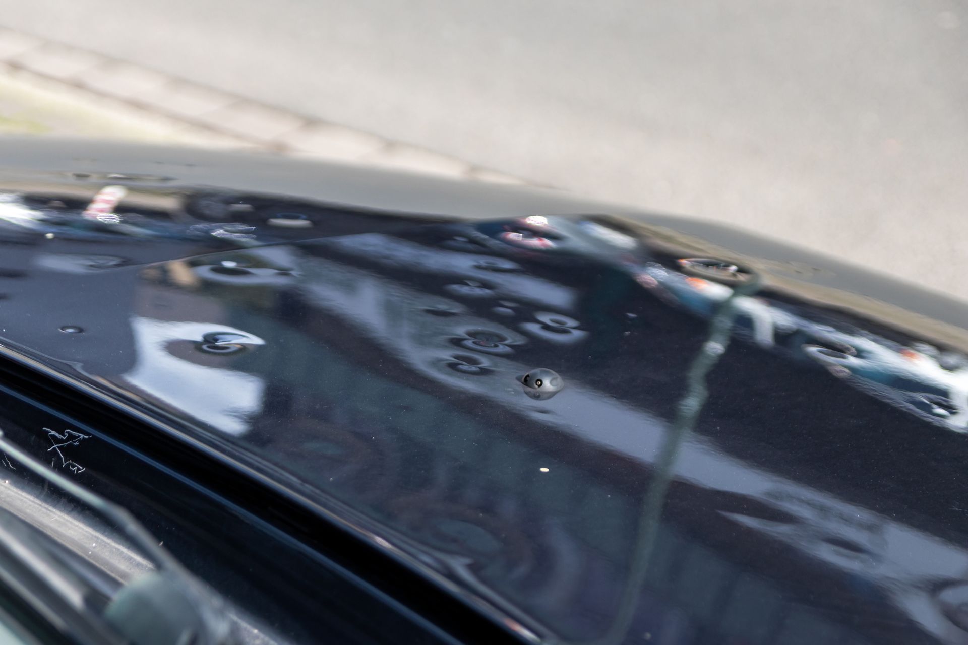 Black car hood with many hail damage dents, showcasing the need for hail damage auto repair.