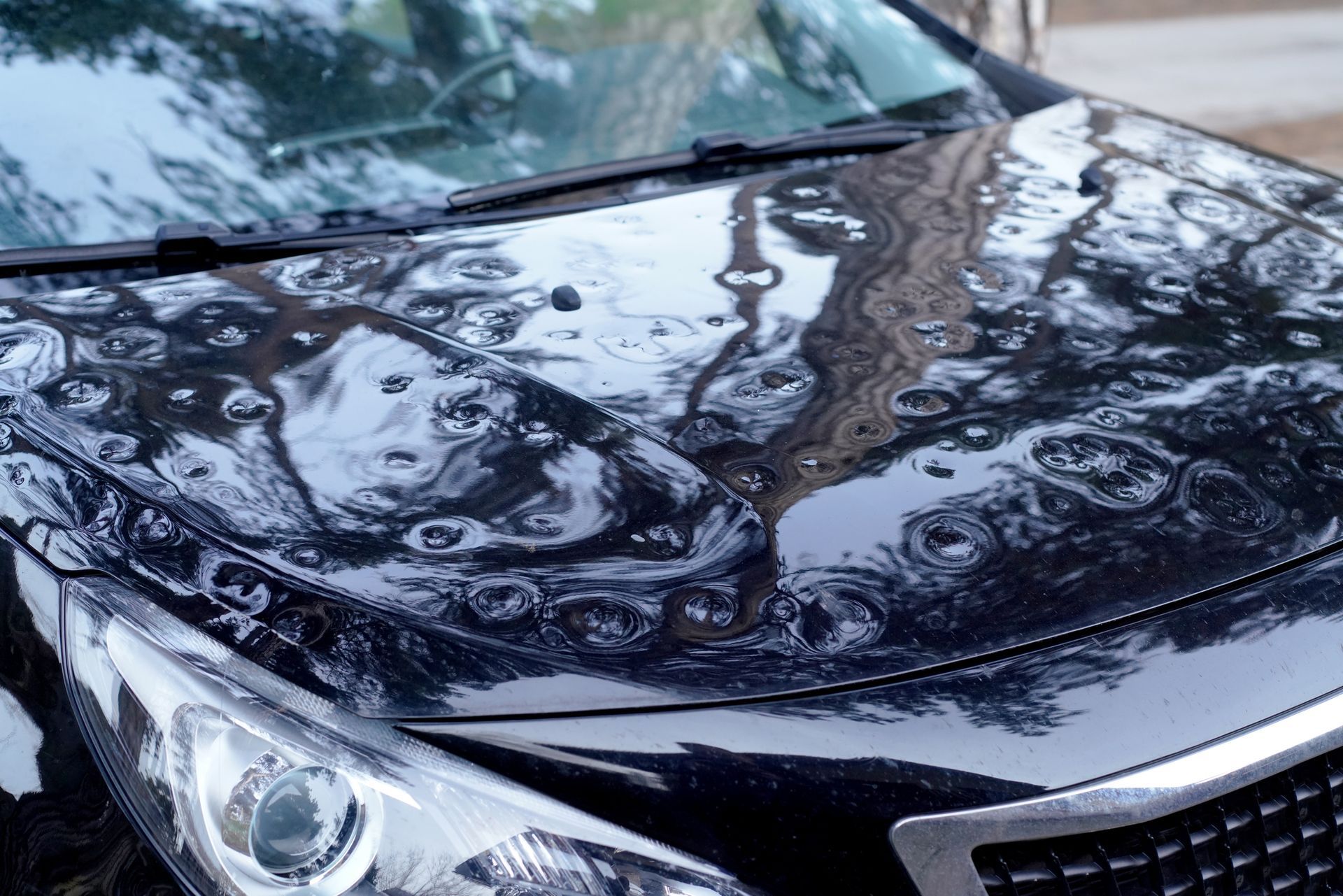 A close-up view of a black car hood with multiple dents caused by a hailstorm.