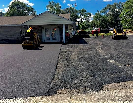 Asphalt paving in progress: Workers, machines, and building with new black asphalt.