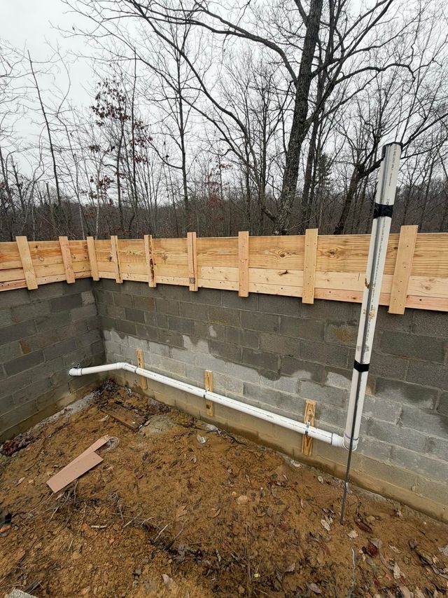 A white PVC pipe runs horizontally along a gray concrete block wall, connecting to a vertical pipe reaching upward.