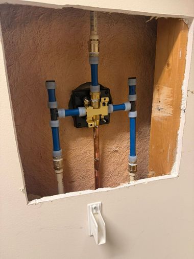 A shower valve rough-in mounted inside a wall cavity with blue and white plumbing pipes connected to a brass fixture.