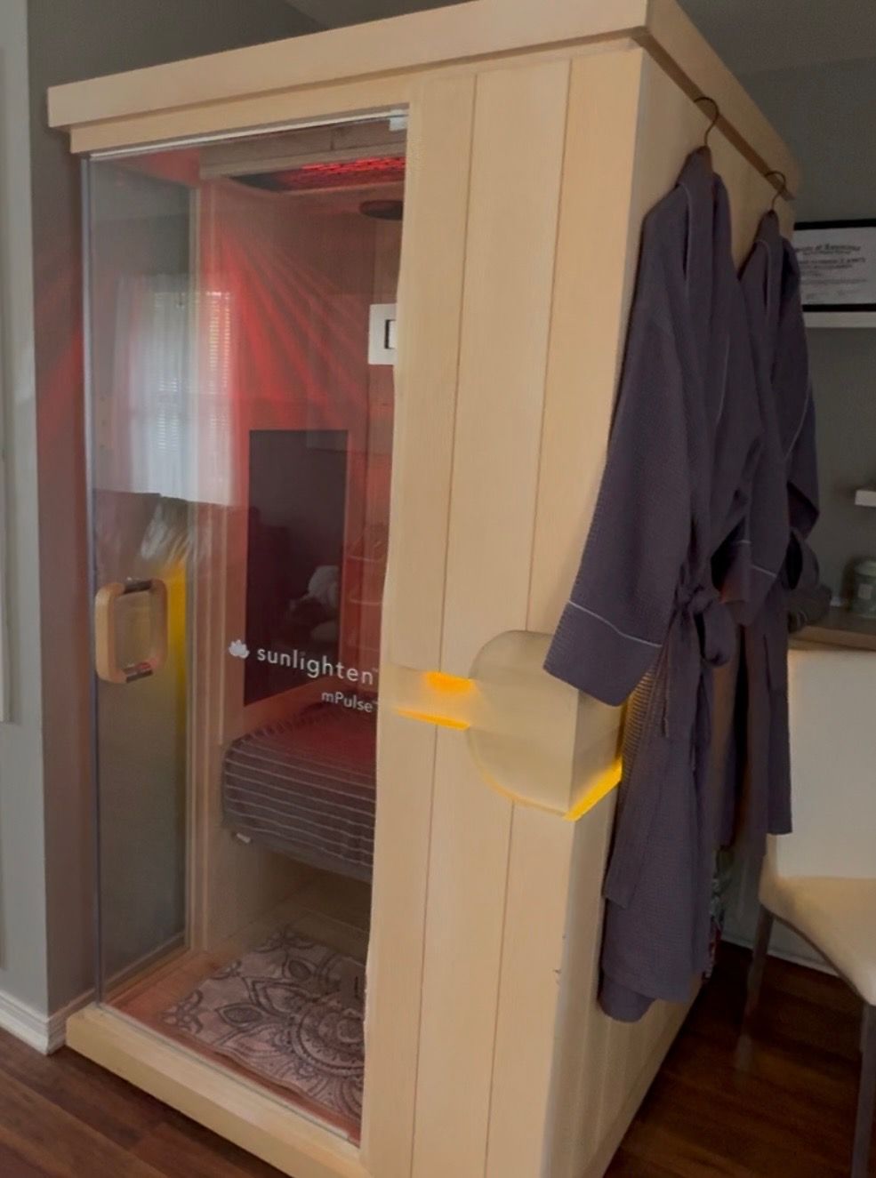 Light wood sauna with glass door and red interior lighting; two robes hang on the side.