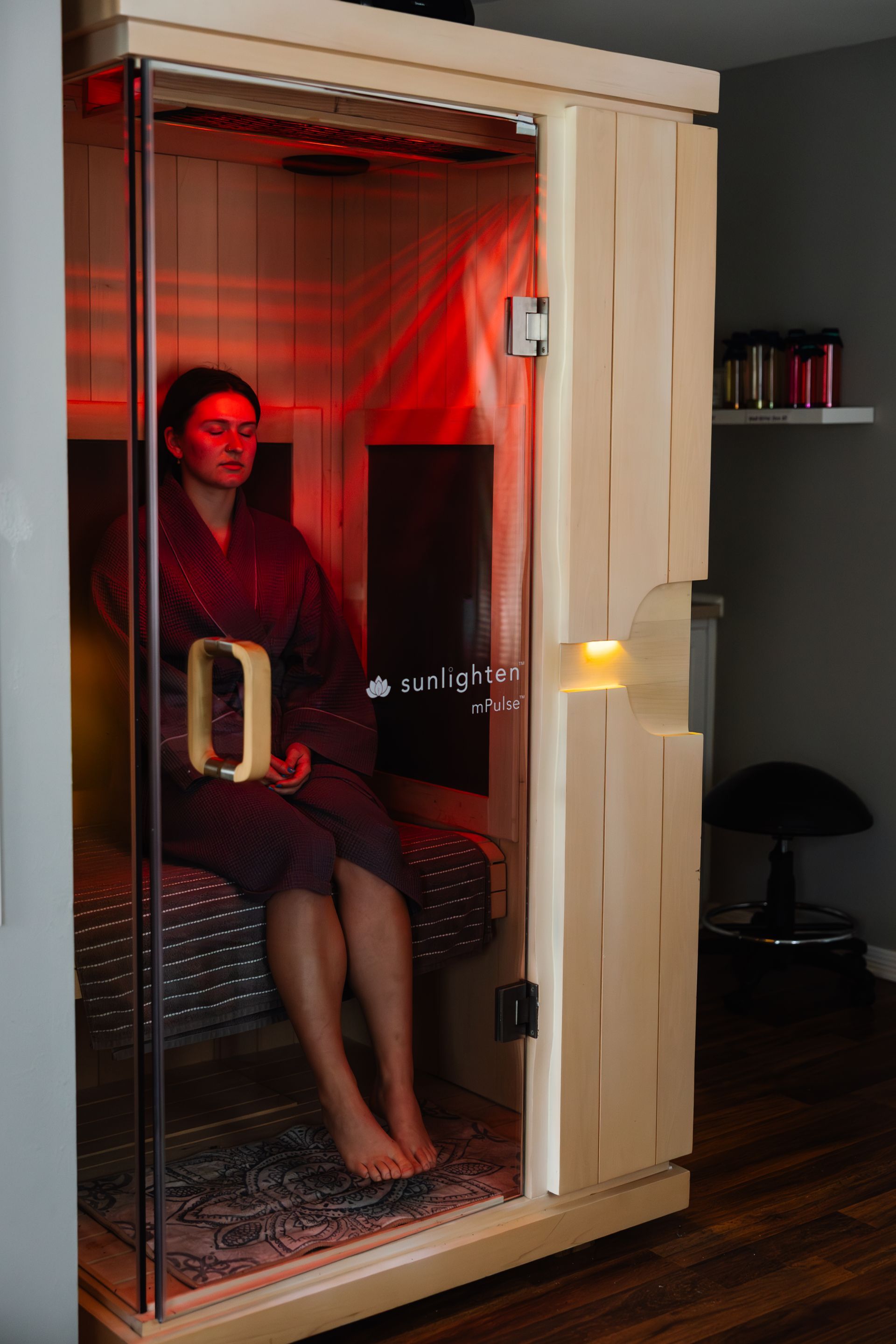 Light wood sauna with glass door and red interior lighting; two robes hang on the side.