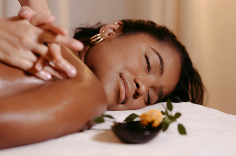 Person receiving shoulder massage at spa. Dark skin, eyes closed, bowl with flower.