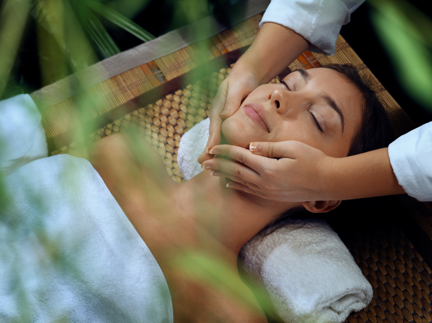 Woman receiving facial massage at a spa; hands on face, eyes closed.