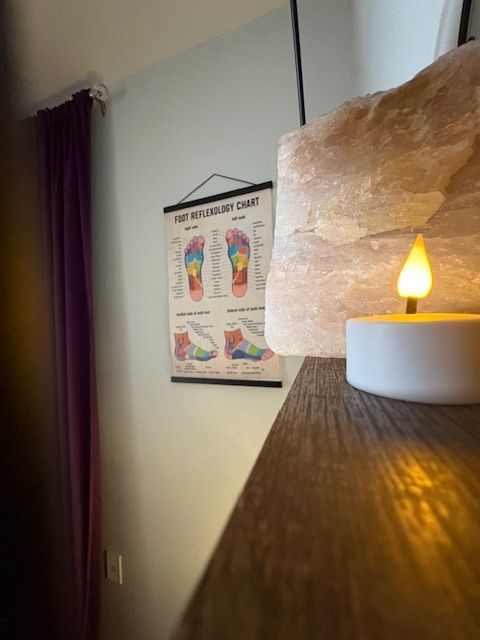 A foot reflexology chart hangs on a wall next to a lit candle and a pink salt lamp.
