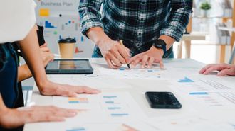 a group of people are sitting around a table looking at charts and graphs .