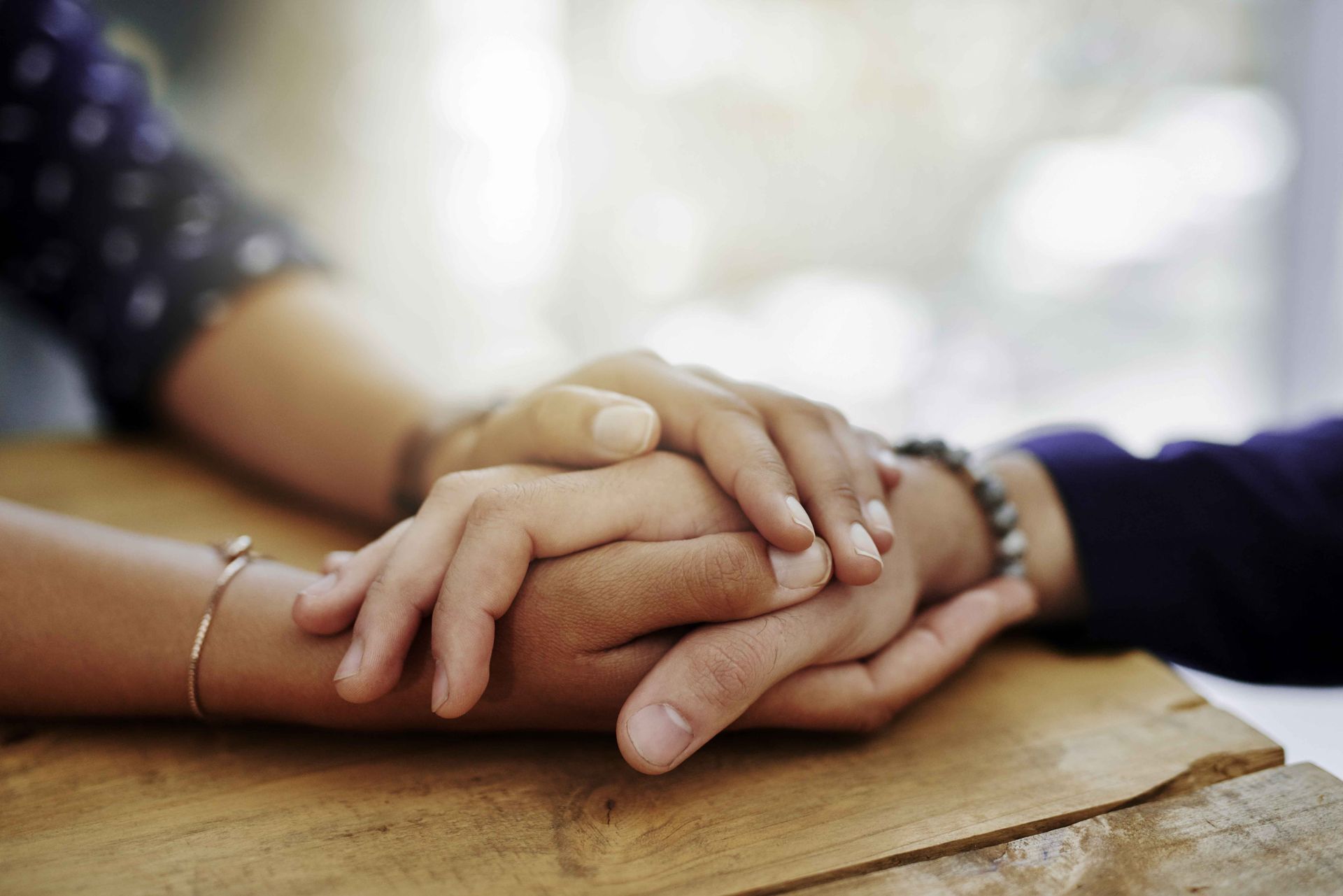 Family of four embraces in a park. Woman in brown jacket smiles, surrounded by three children.