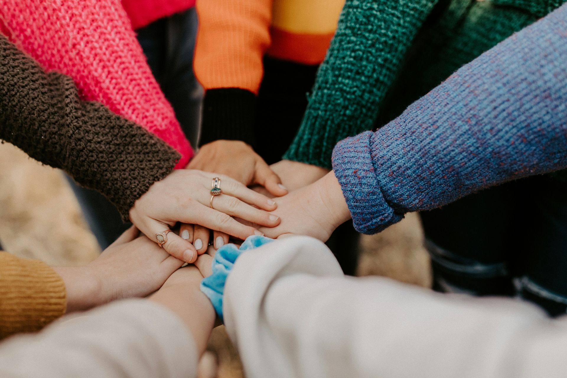 Several people in colorful sweaters stack their hands together in a display of unity.