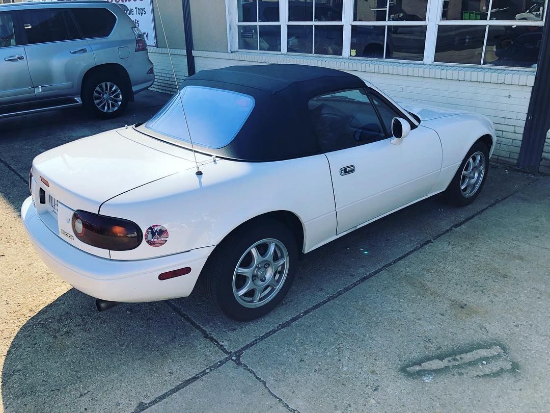 A white sports car with a black top is parked on the side of the road.