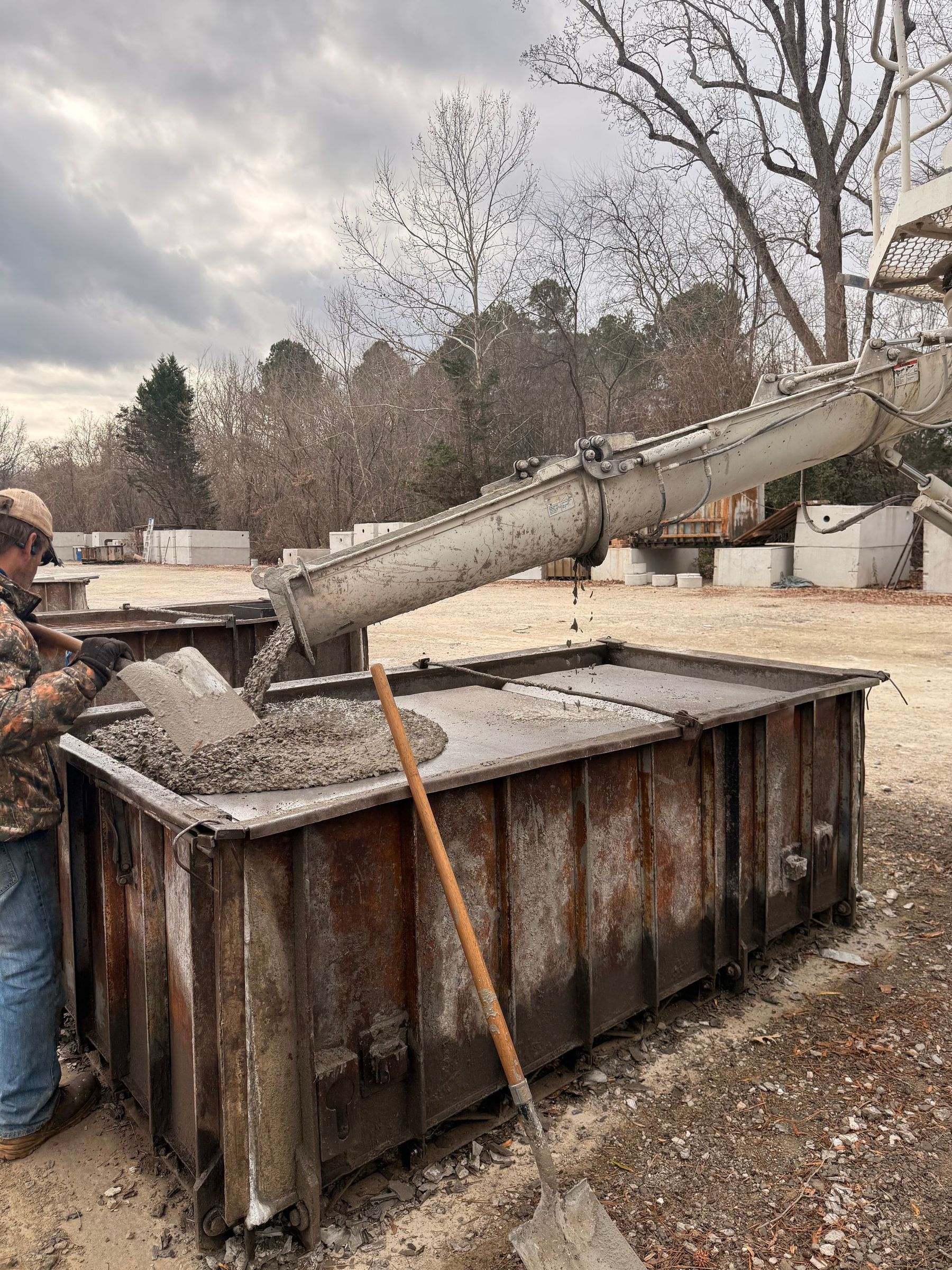 Open concrete drain with standing water, surrounded by dirt and plumbing pipes.