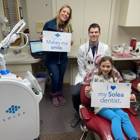 Dentist, patient, and woman hold signs in dental office. 

