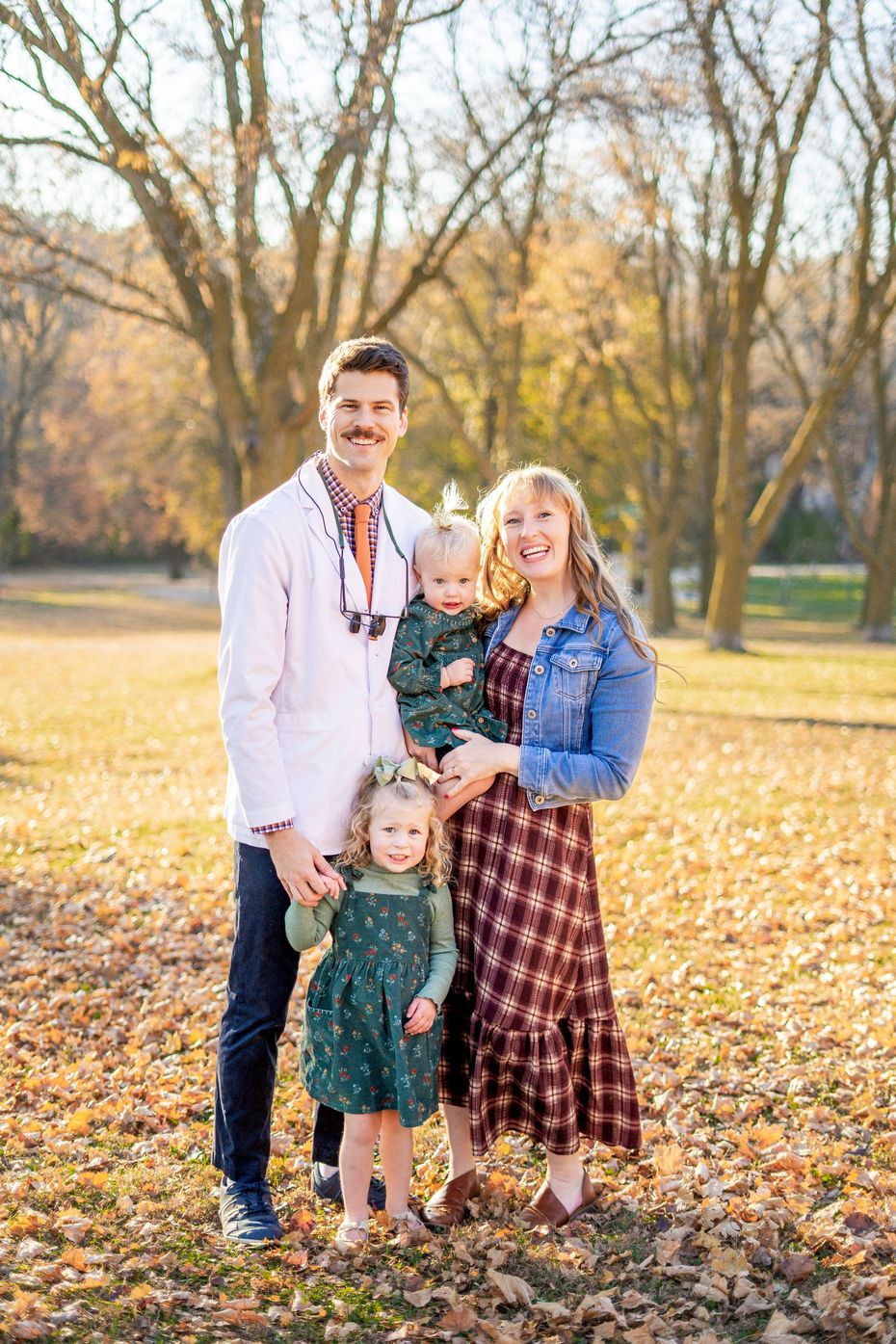Family of four smiling outdoors in fall leaves.