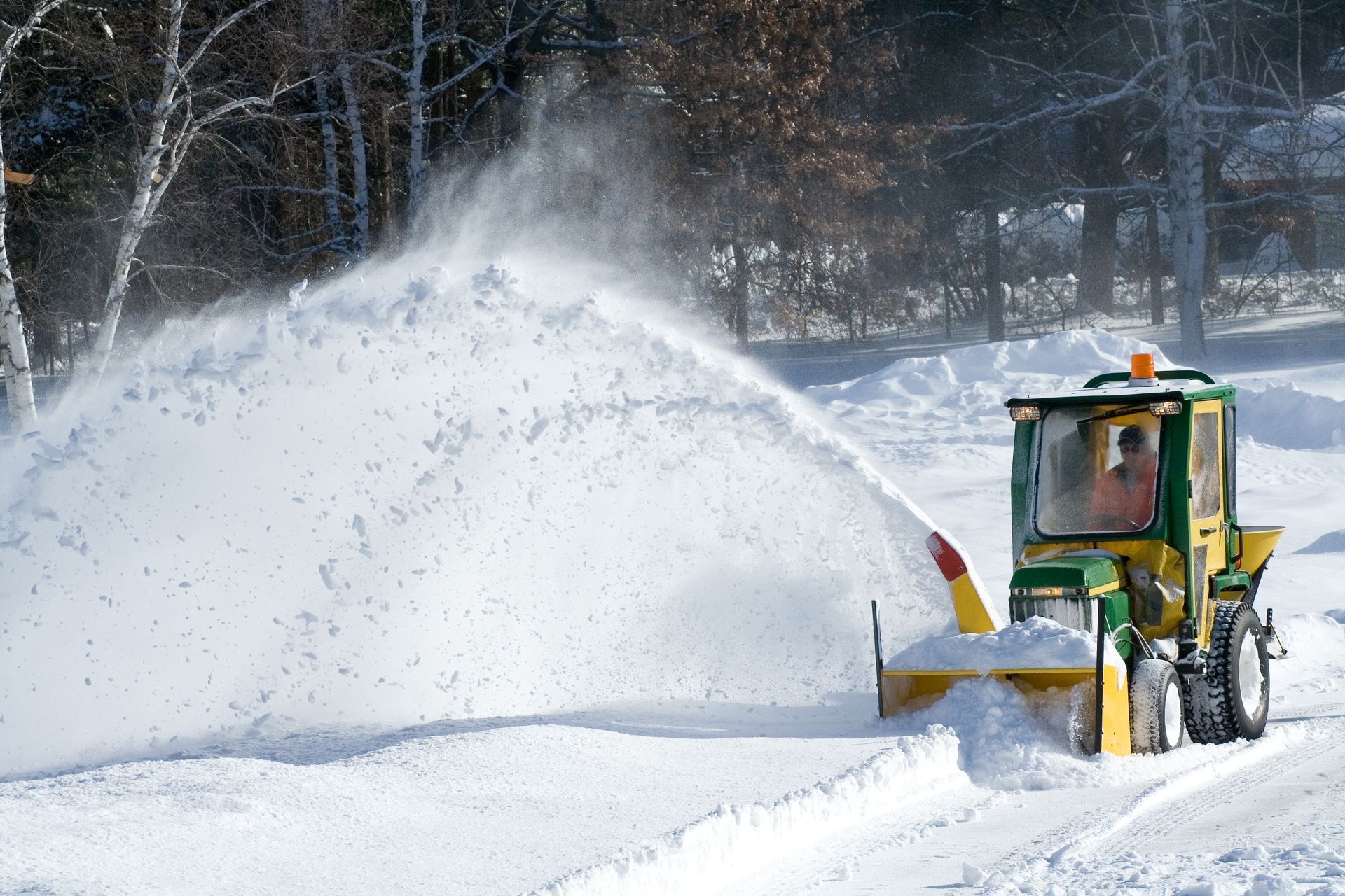 A snow blower is blowing snow on a snowy road