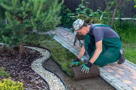 A man is kneeling down to roll out a roll of grass in a garden.