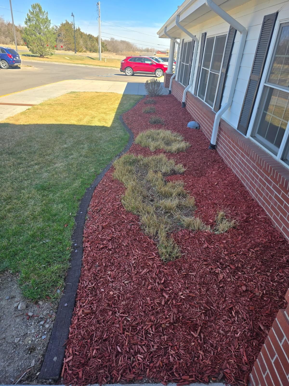 A brick building with brown mulch landscaping containing patches of dormant yellow grass along the foundation.