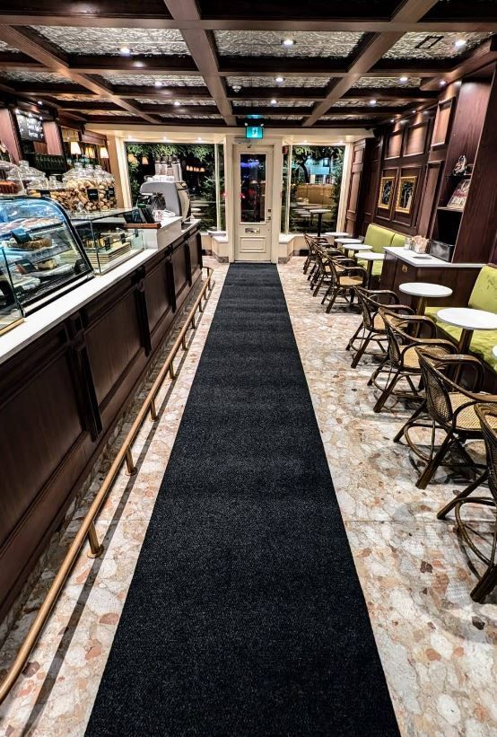 A long black carpeted hallway leading to a restaurant with tables and chairs.