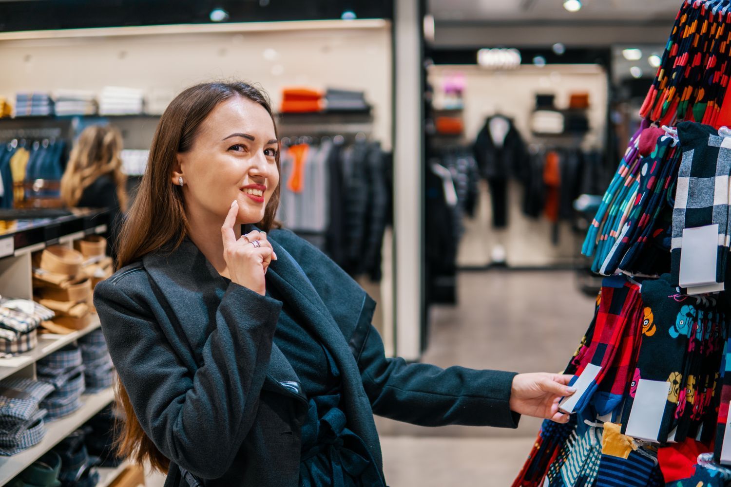 Woman shopping in a store, looking at socks, smiling, hand to her chin.