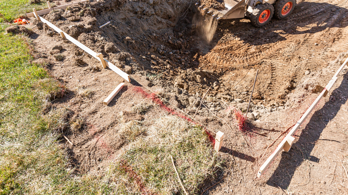 A construction site with a small excavator digging in dirt within a wooden frame.